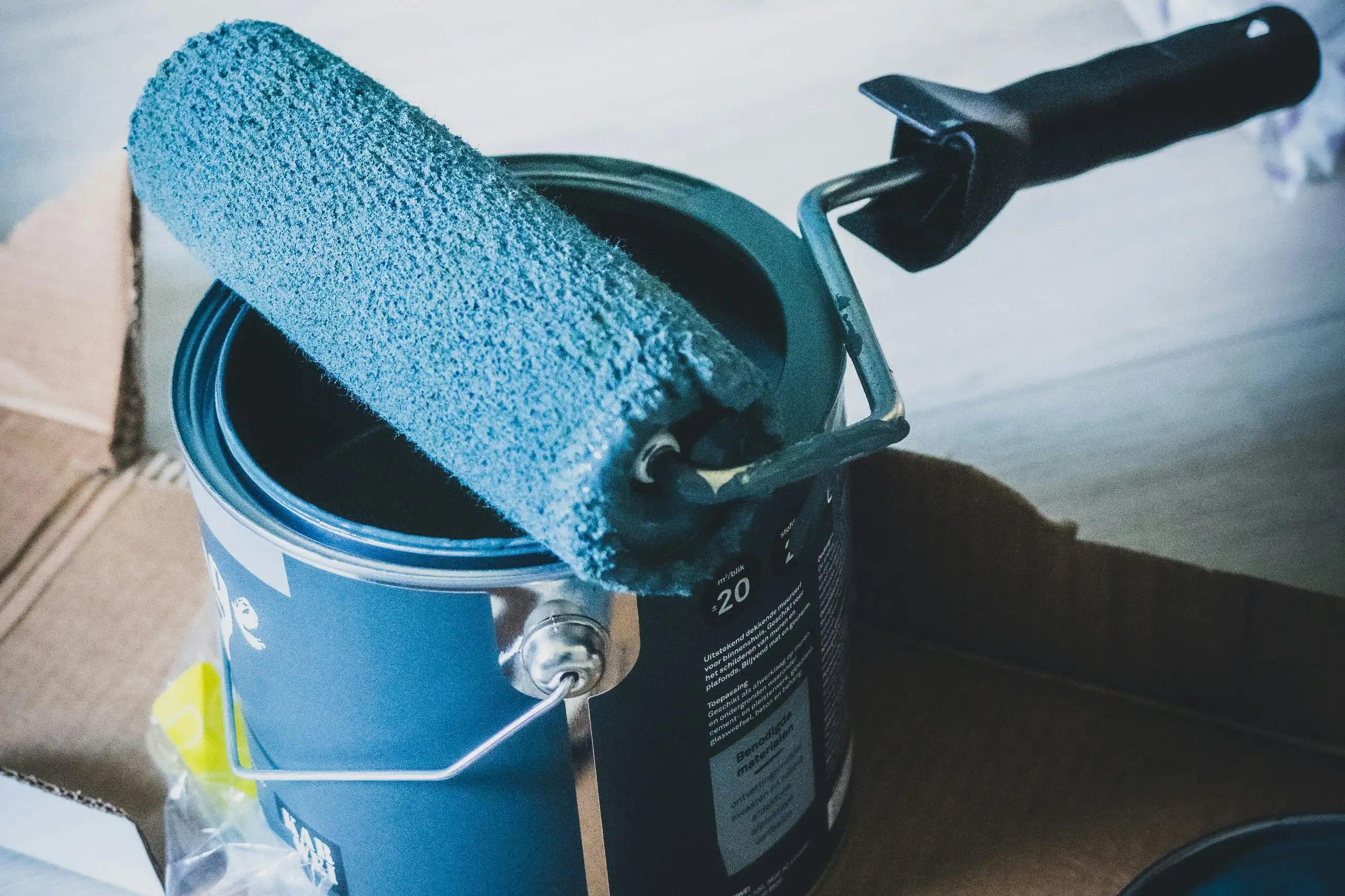 A blue paint roller resting on an open tin of paint