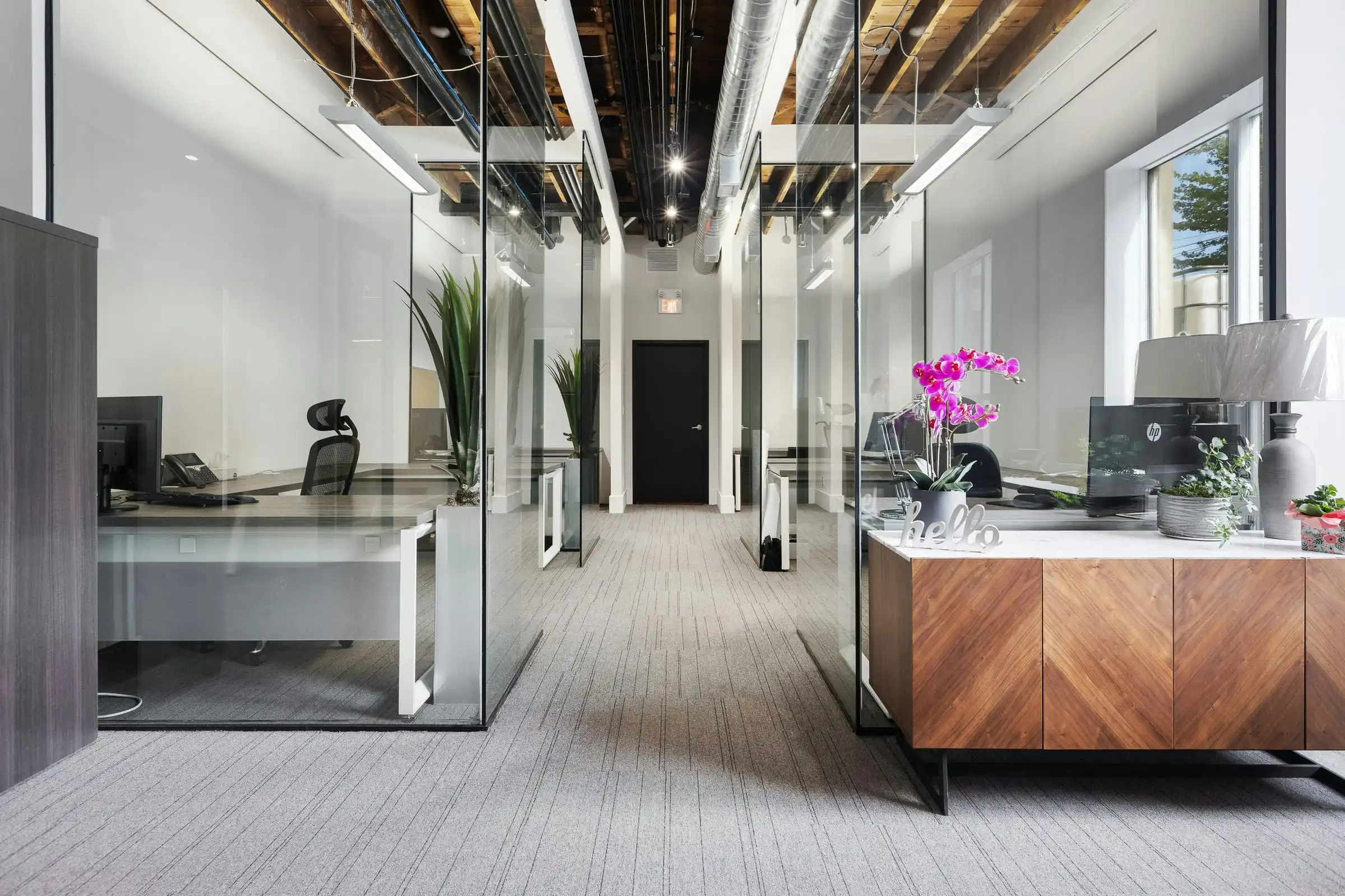 An office corridor with glass-walled rooms, white walls and a timber reception desk