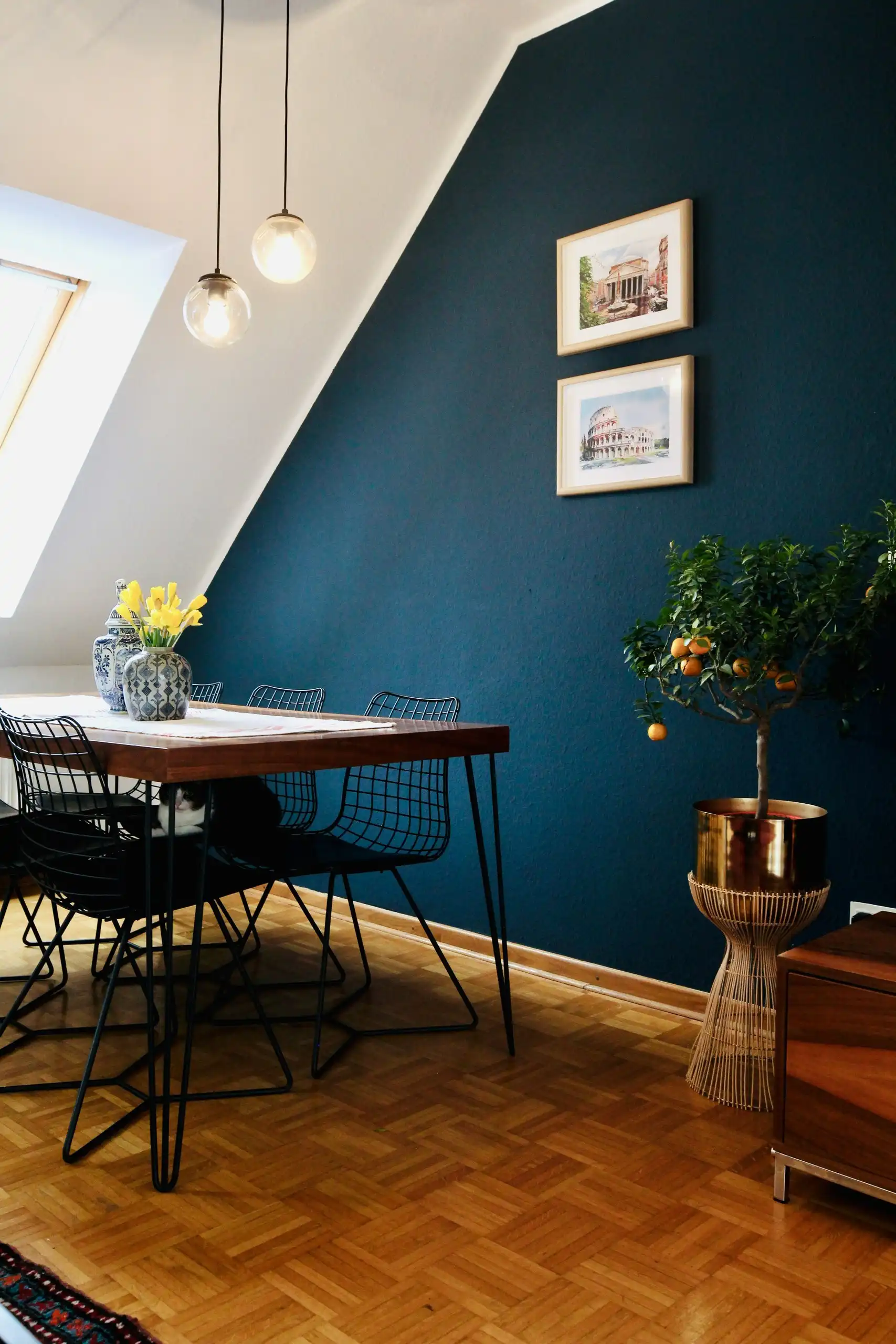 A dining corner under a sloping ceiling, one wall painted deep navy behind framed prints
