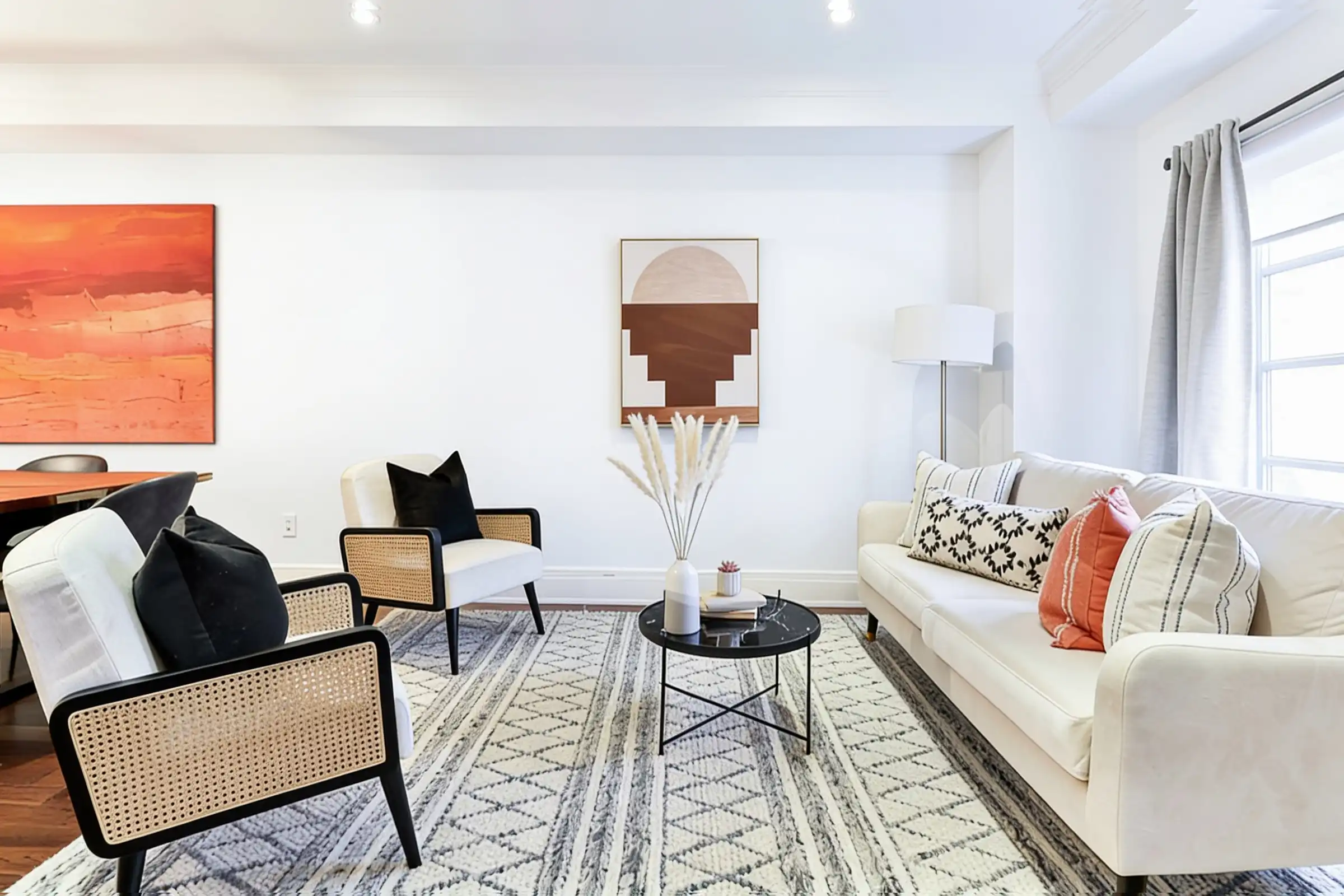 A living room with plain white walls, a cane armchair, a white sofa and a large orange painting