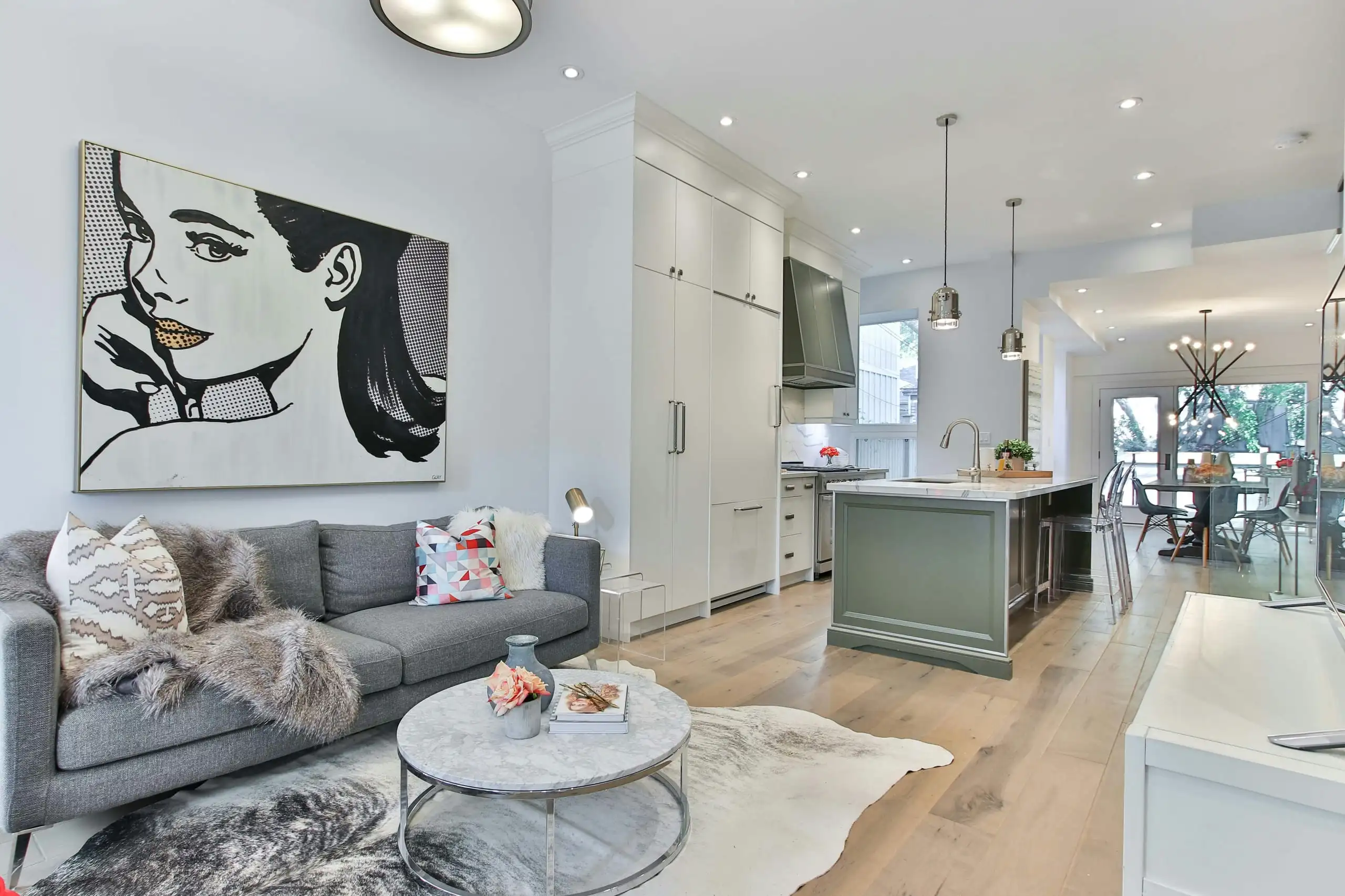 An open-plan living room and kitchen with white walls, a pop-art print and a grey sofa
