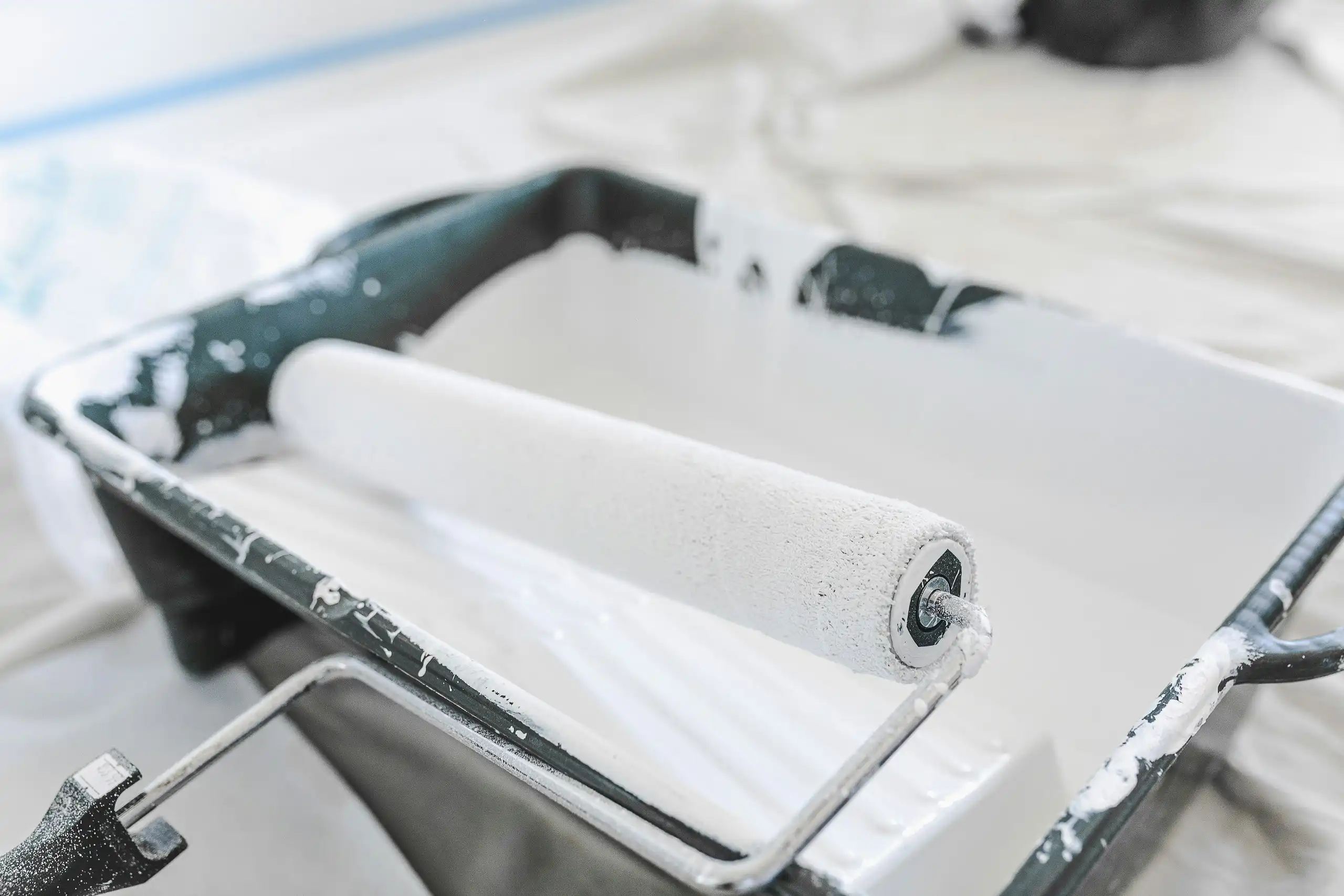 A paint roller resting in a tray of white paint