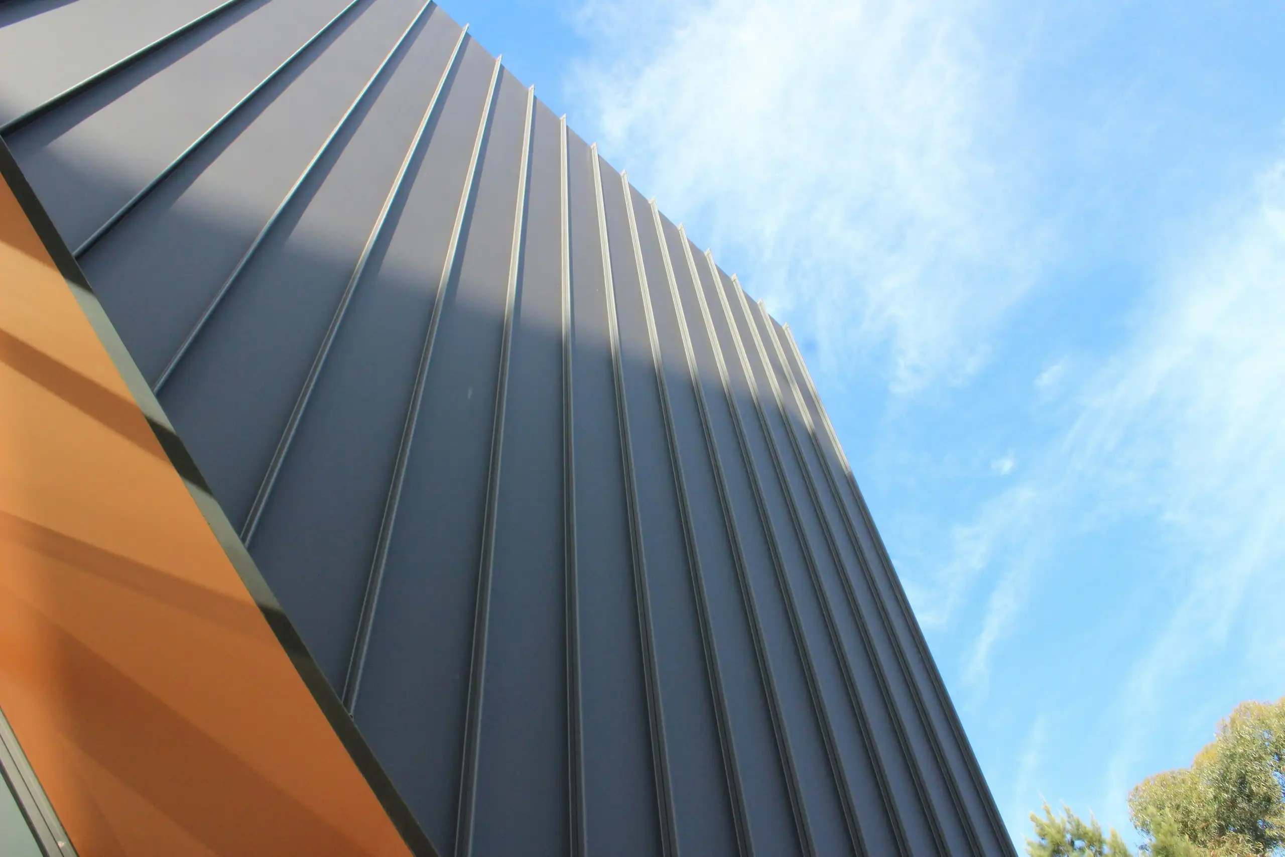 A dark grey metal roof with standing seams, against a blue sky
